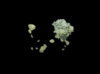 Einige gelbliche Kristalle sowie zeriebene Kristalle auf schwarzem Hintergrund