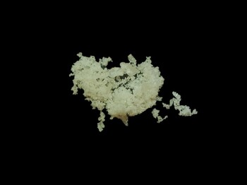 Leicht gelbliches, kristallines Pulver auf schwarzem Hintergrund